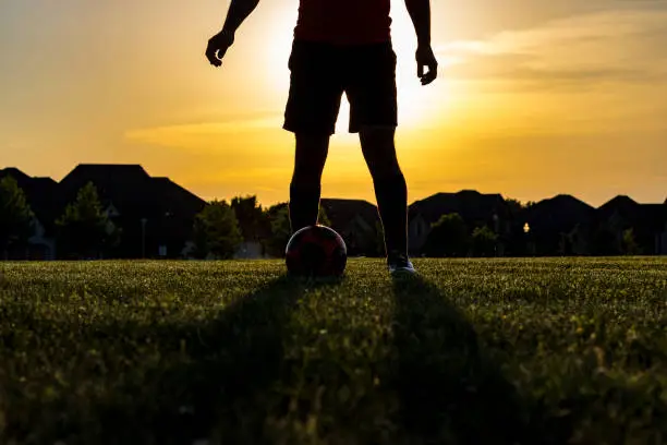 Silhouette of soccer player in a public park shot against the sun creating an epic halo in the background.