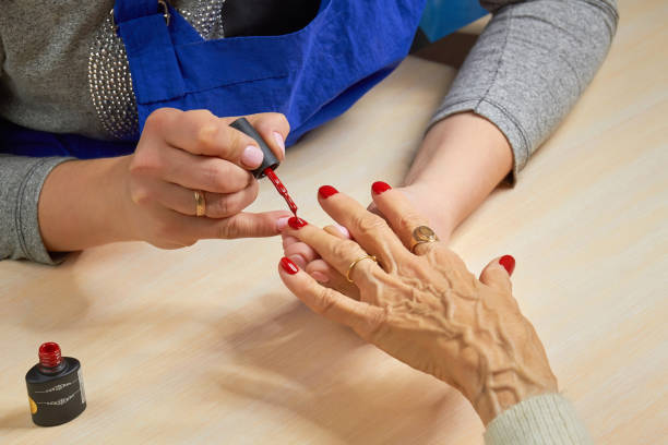 Beautician applying red varnish to woman nails. Beautician applying red varnish to woman nails. Manicurist painting nails to elderly woman with red polish on salon table. Old woman receiving manicure. manicure stock pictures, royalty-free photos & images