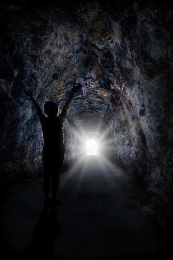 Silhouette of woman raising hands with blinding light at the end of the tunnel. Concept of light at the end of the tunnel such as conquering adversity or success through obstacles.