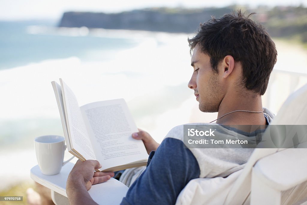 Homem com copo de café ler um livro na Cadeira de Recosto esquecendo - Royalty-free Praia Foto de stock