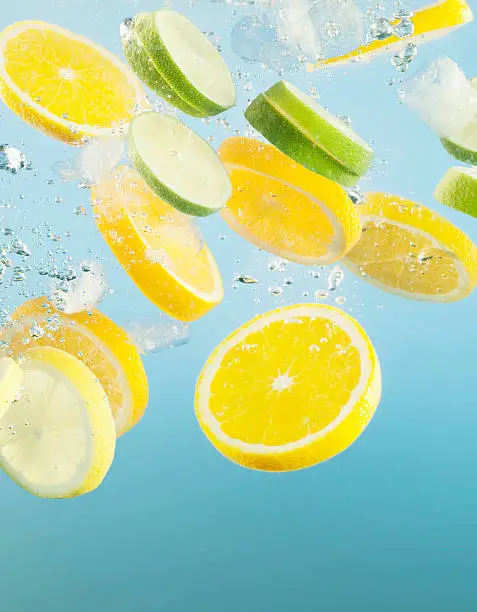 Photo of Close up of sliced lemons and limes splashing in water