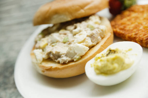 tuna salad on a bagel with hash brown deviled egg and strawberry on a white plate - tuna tuna salad bagel sandwich imagens e fotografias de stock