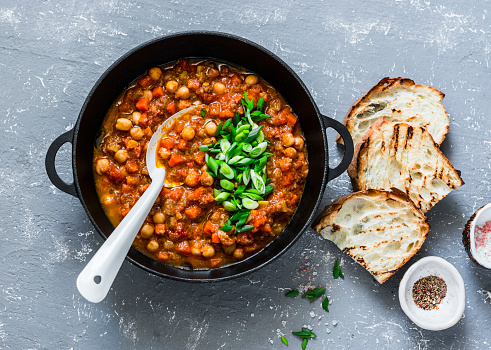 Vegetarian mushrooms chickpea stew in a iron pan and rustic grilled bread on a gray background, top view. Healthy vegetarian food concept. Vegetarian chili