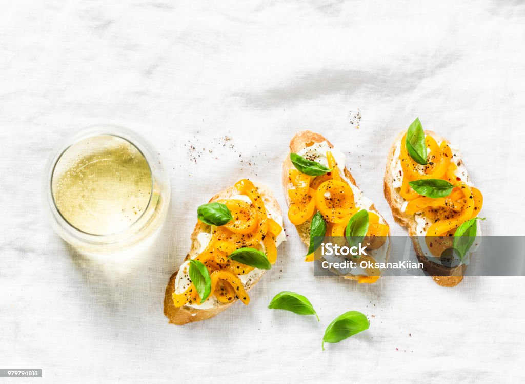 Cream cheese, roasted yellow bell pepper, basil bruschetta and white  wine on light background, top view. Flat lay, copy space Aperitif Stock Photo