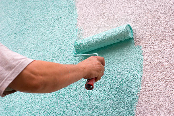 Male worker painting a white wall painting wall with a roll in green outdoor Stucco stock pictures, royalty-free photos & images