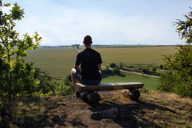 istock Young man sitting on bench on nature lookout, Czech landscape 979856696