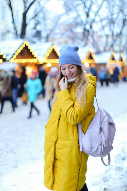 istock Young female student wearing yellow coat, backpack and cap walking on snow 979872326