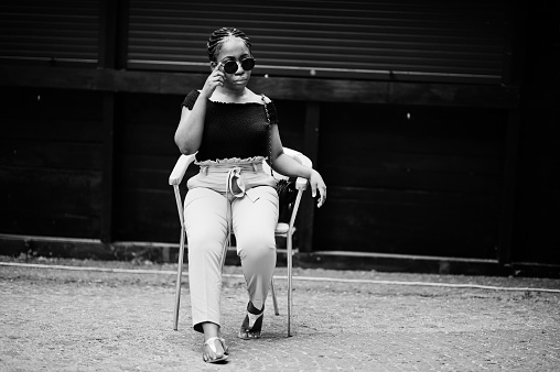 Stylish african american woman in sunglasses posed outdoor at chair.