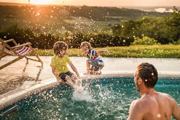 Photo of Happy boys having fun while being splashed by their father from the swimming pool.