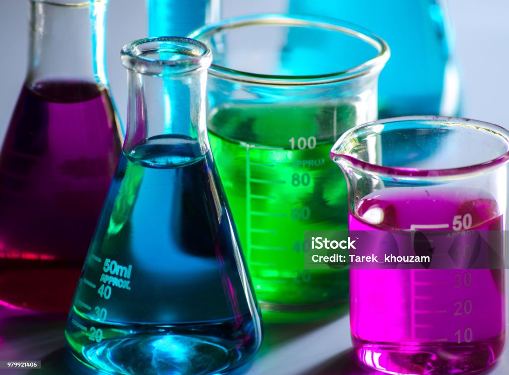 Chemical glass tools in laboratory Conical flasks , beakers , and measuring cylinder containing colored solutions on a white background Chemical Stock Photo