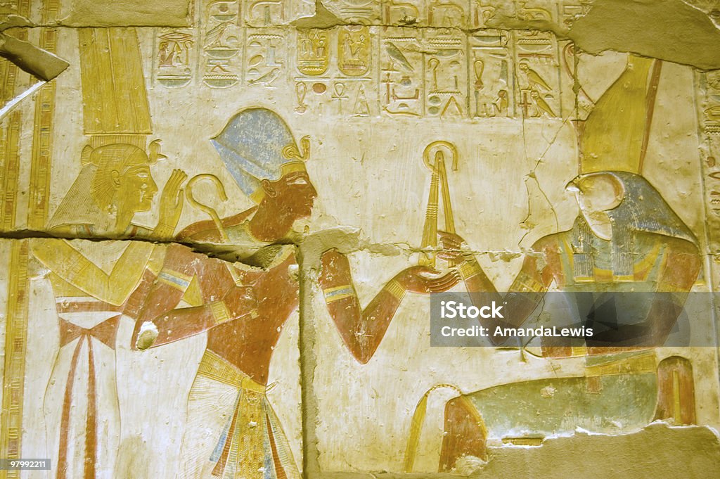 Ancient Egyptian god Horus with Seti and Isis An ancient egyptian hieroglyphic painted  carving showing the falcon headed god Horus seated on a throne and holding a golden fly whisk.  Before him are the Pharoah Seti and the goddess Isis.  Interior wall of the temple to Osiris at Abydos, Egypt. Osiris Stock Photo