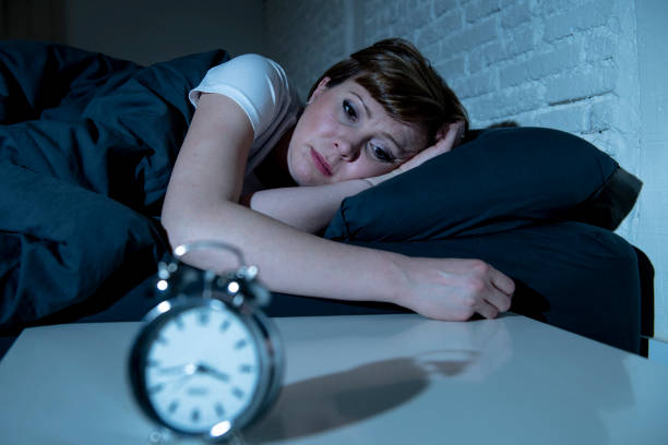 Young attractive red haired caucasian woman lying in bed late at night trying to sleep suffering from insomnia, nightmares or sleeping disorders. looking stressed and exhausted. stock photo