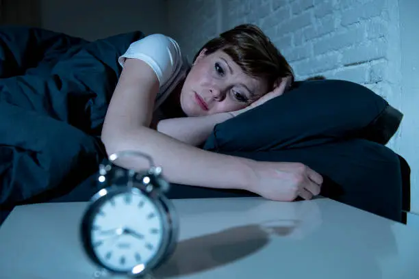 Photo of Young attractive red haired caucasian woman lying in bed late at night trying to sleep suffering from insomnia, nightmares or sleeping disorders. looking stressed and exhausted.