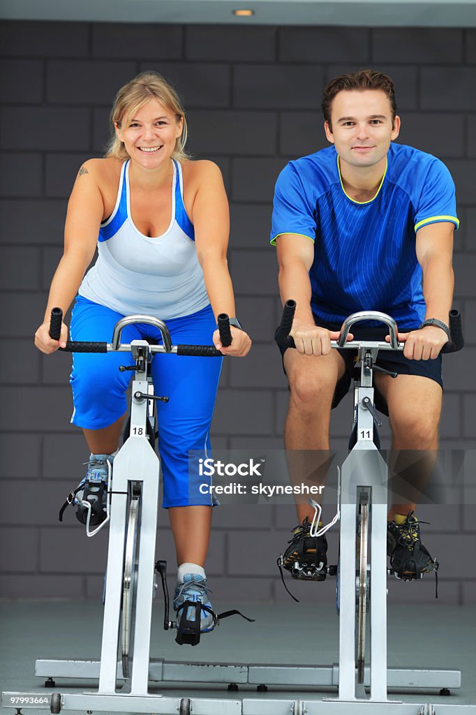 Man and woman exercising on bicycles in a gym. - Royalty-free Sportschool Stockfoto