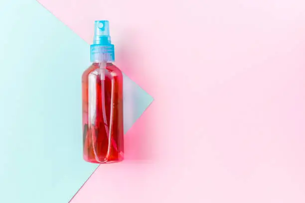 Spray water of red color in  bottle for protection skin and hair care. On a pink and blue background, copy space