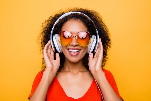 Head shot portrait of cheerful positive girl in summer glasses with headphones on head listening favorite pop music isolated on yellow background