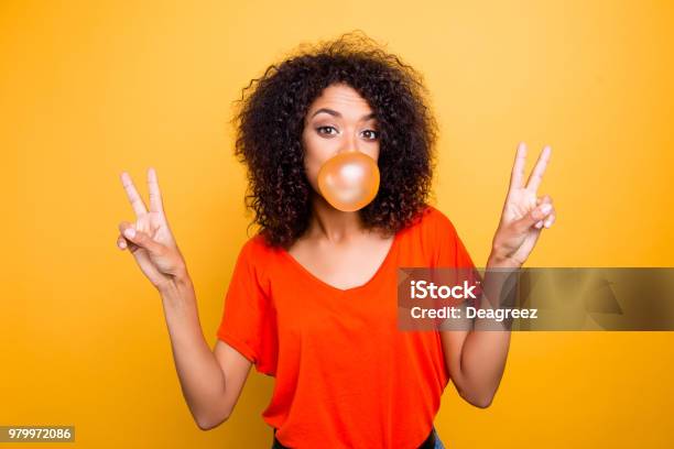 Portrait Of Cheerful Cool Girl With Modern Hairdo Blowing Chewing Bubble Gum Gesturing Vsigns With Two Hands Looking At Camera Isolated On Yellow Background Stock Photo - Download Image Now