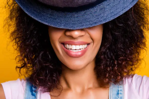 Photo of Closeup cropped portrait of cheerful positive girl with white straight teeth hiding half face with hat isolated on yellow background
