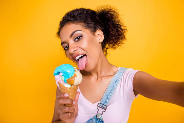 autoportret dziewczyny o lody waniliowe w stożek wafel lizanie z językiem obecnie fotografowania selfie na przedniej kamery izolowane na żółtym tle - ice cream cone ice cream vanilla ice cream isolated zdjęcia i obrazy z banku zdjęć