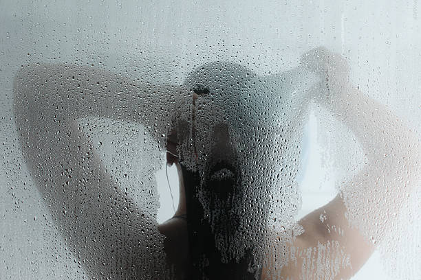silhouette of woman taking shower behind steamy door - douchen stockfoto's en -beelden