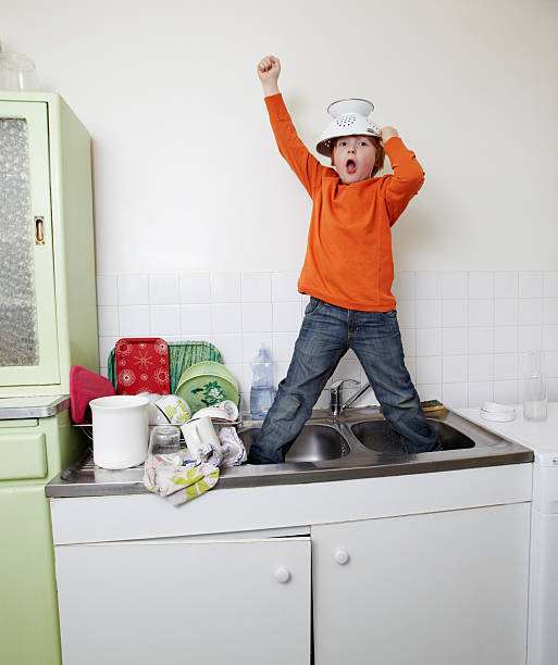 boy standing in sink with colander helmet boy, kitchen, dishes, sink, colander, orange sweater, at home child behaving badly stock pictures, royalty-free photos & images