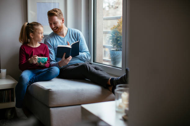 istock Father and daughter reading together near the window 980012082