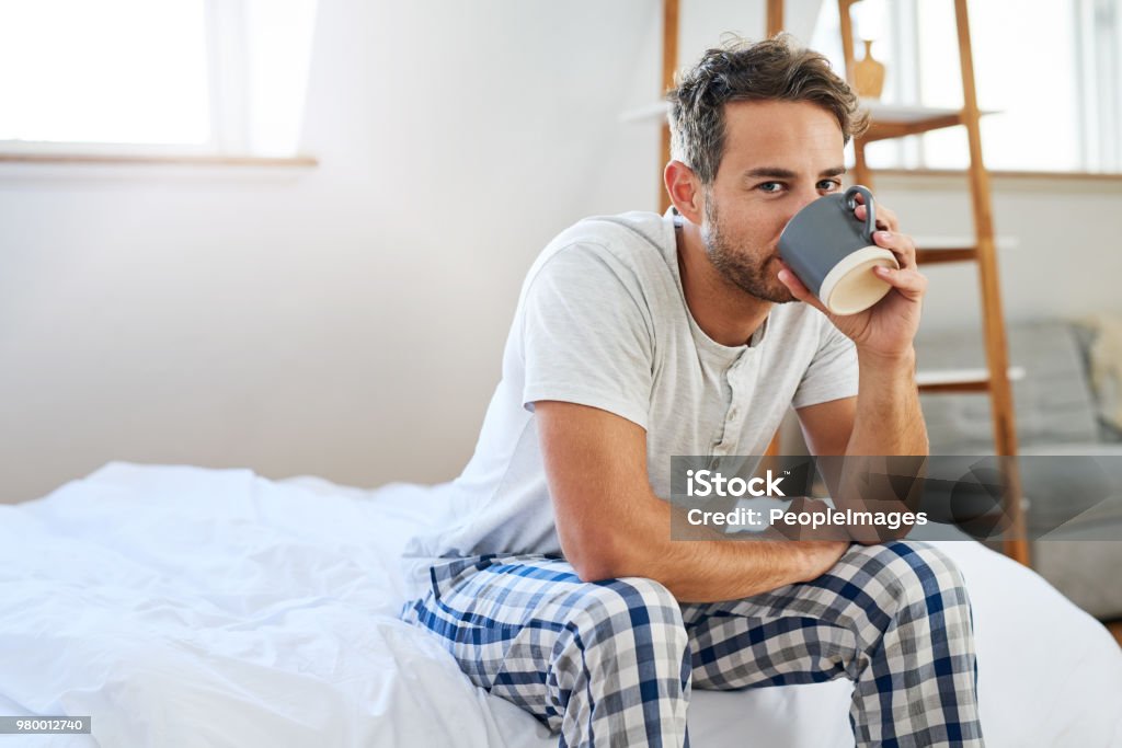 The day doesn't start until that first sip Shot of a handsome young man drinking coffee in bed at home Men Stock Photo