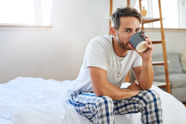 The day doesn't start until that first sip Shot of a handsome young man drinking coffee in bed at home pajamas stock pictures, royalty-free photos & images