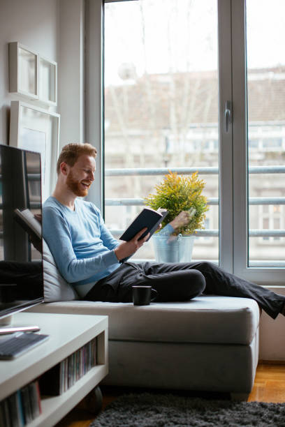 istock Man reading book near the window 980018508
