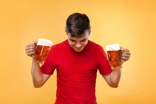 Young fit man at Beer Fest, drinking beer on yellow background.
