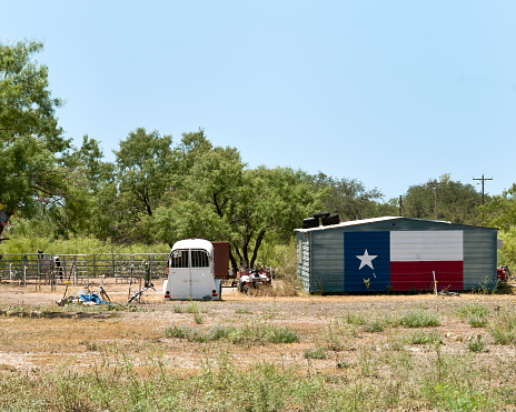 Metal building with Texas Flag painted on its side along with horse trailer in Texas Pasture.