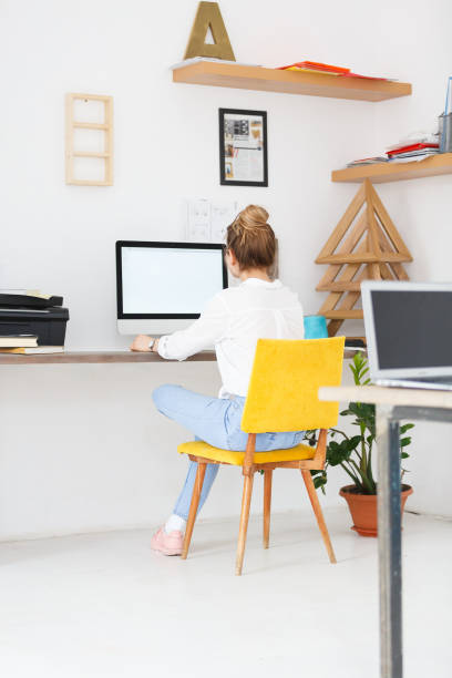 istock Back view of young female freelancer work in office, sits at desk in modern creative studio, using digital computer, reads information on web page, surfing websites. Job, career, profession concept. 980041034