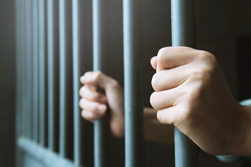 Hombre en la prisión de las manos de detrás espera jaula de acero barras de cárcel. Penal del delincuente encerrado en la cárcel. photo