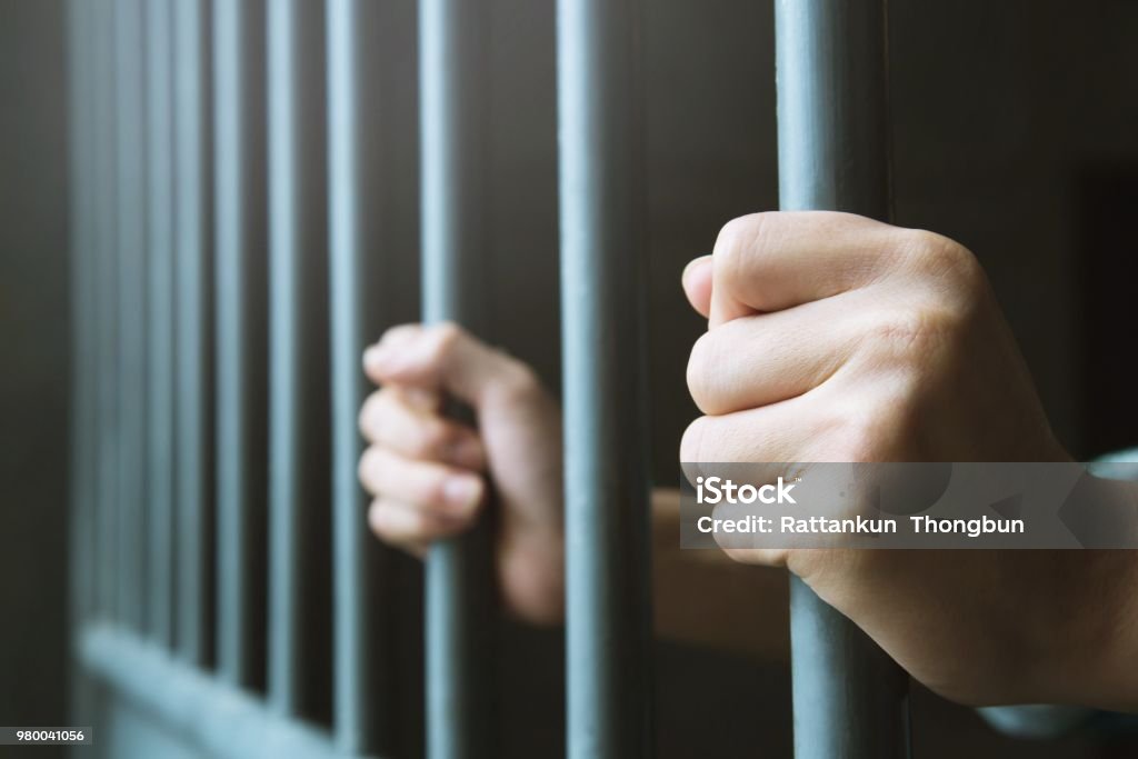 Man in prison hands of behind hold Steel cage jail bars. offender criminal locked in jail. Prison Stock Photo