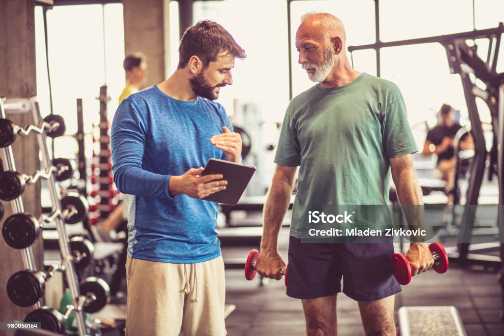 Love for healthy life. Senior man and fitness instructor talking in gym. Fitness Instructor Stock Photo