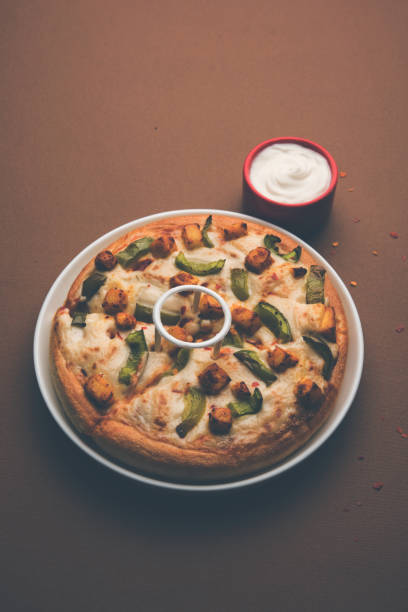 paneer pizza to indyjska wersja włoskiego dania z dodatkiem twarogu, podawana na talerzu z białym sosem. selektywne skupienie - cheeze zdjęcia i obrazy z banku zdjęć