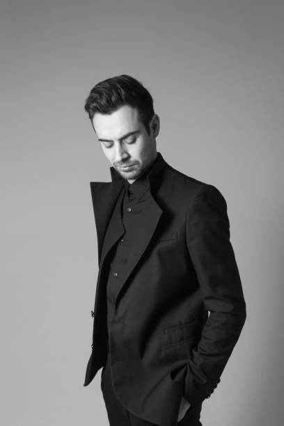 istock Young handsome man in a black suit, standing, looking down 980058564