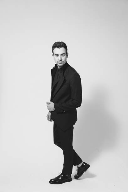 istock Young handsome man in a black suit, standing, seriously looking at the camera 980061330