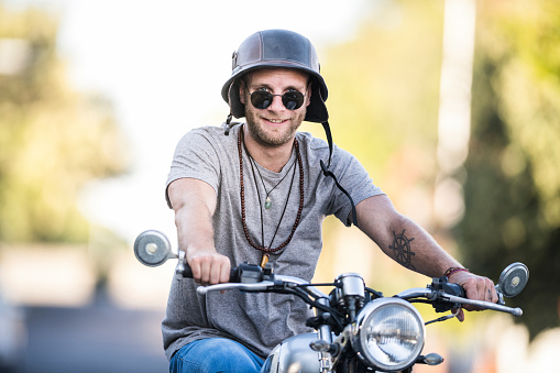 Portrait of mid adult man riding motorcycle. Confident male is smiling while wearing helmet. He is wearing casuals in city.