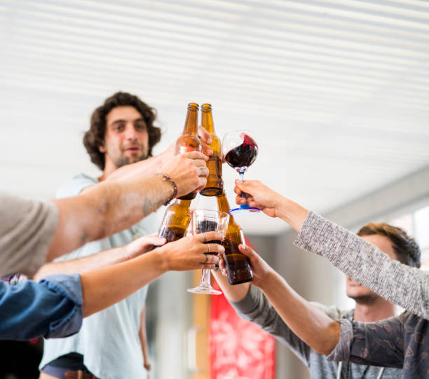 Male and female friends toasting alcohol glasses and bottles. Multi-ethnic men and women are enjoying at social gathering. They are at home.