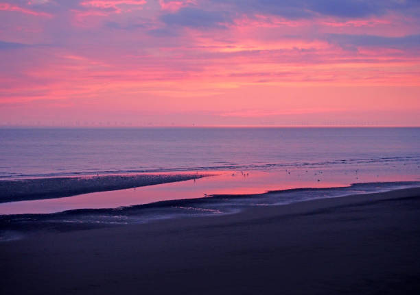 beautiful twilight dramatic purple sky over the sea with dramatic colourful evening clouds reflected in calm water and dark beach