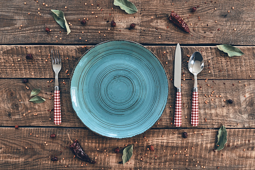 High angle shot of empty plate, fork, spoon, knife lying on rustic table