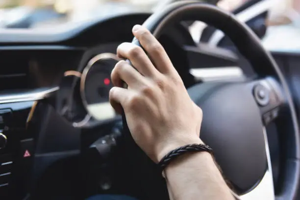 Photo of Male arms holding leathern rudder of car