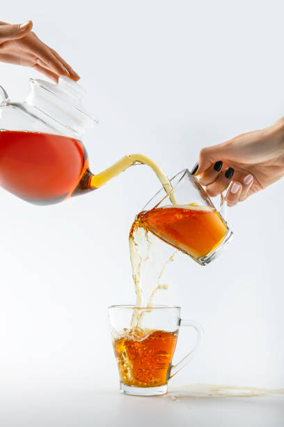 cropped image of hands pouring tea from teapot in cups isolated on white