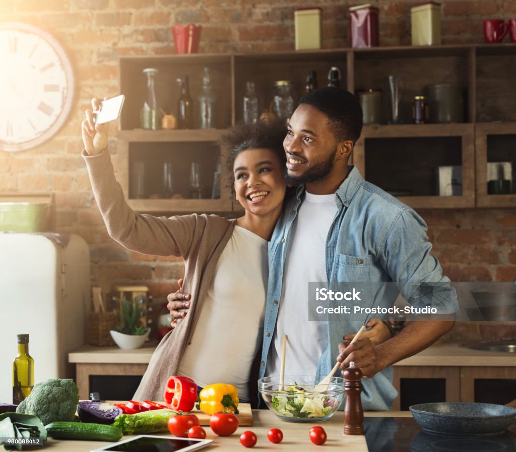 Happy black couple taking selfie at kitchen Happy black couple taking selfie with smartphone while preparing healthy salad at kitchen Cooking Stock Photo