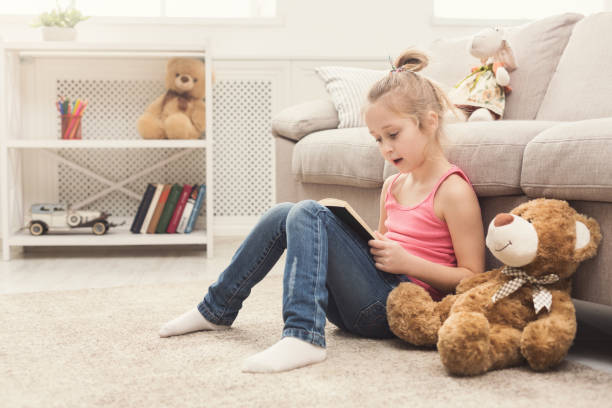 istock Lttle girl and her teddy bear reading book 980099784