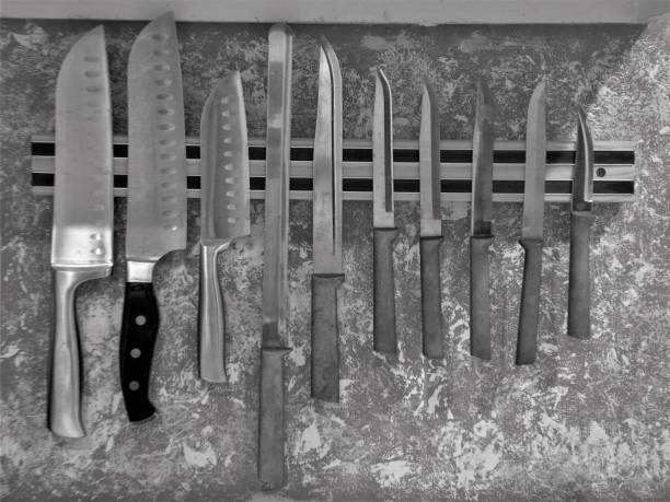 Royalty Free Photograph - Magnetic Knife Bar on the Kitchen Wall - Black and White Image of a Collection of Assorted Kitchen Knives held on a Magnetic Storage Bar - Ten Knives are Ready for the Cook to Use - One of the Ten Knives is Turned the Wrong Way B&W Photograph of Ten Cook's Knives in the Kitchen - The Chef's Knives are hanging on Magnetic Storage Bar - Chef's Knives are on the Wall - Knife Number Nine is turned the Wrong Way - Who Put Knife #9 Backwards? kitchen knife photos stock pictures, royalty-free photos & images