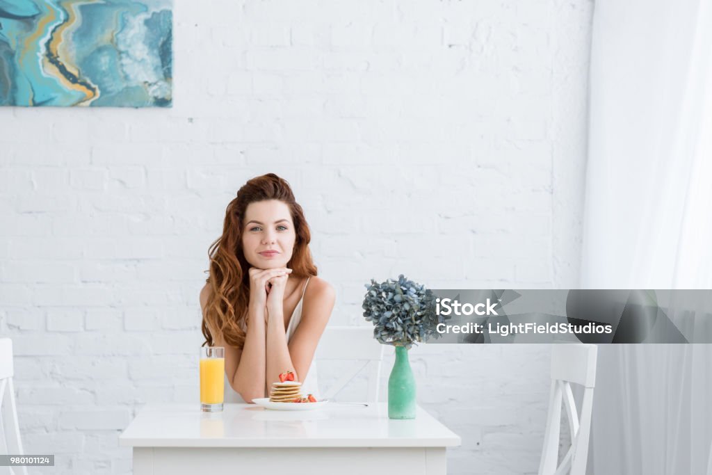 beautiful young woman with orange juice and pancakes with strawberry for breakfast at home looking at camera Adult Stock Photo