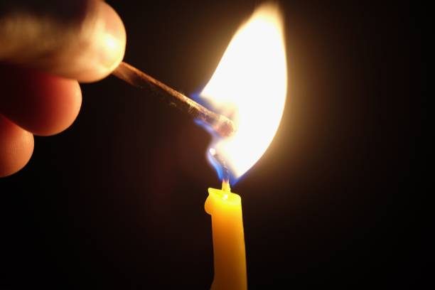 istock hand ignite a yellow candle with match stick on black background 980110970
