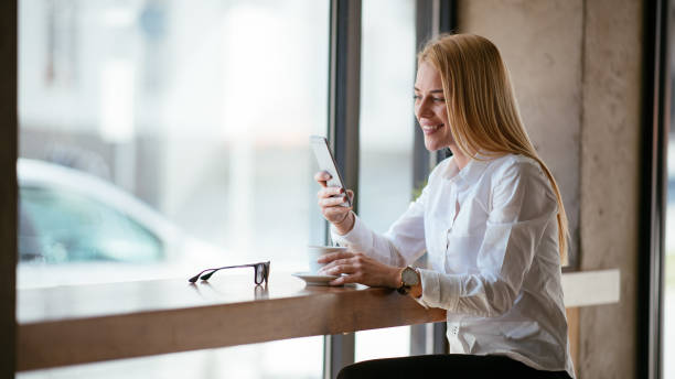 istock Beautiful blond woman drinking coffee and using smartphone 980117198